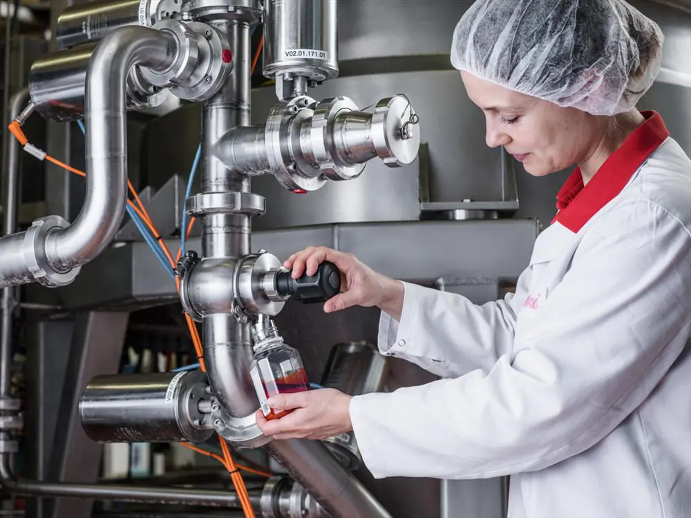 Tecnica di laboratorio preleva un campione di prodotto dalla valvola di un impianto in acciaio inox