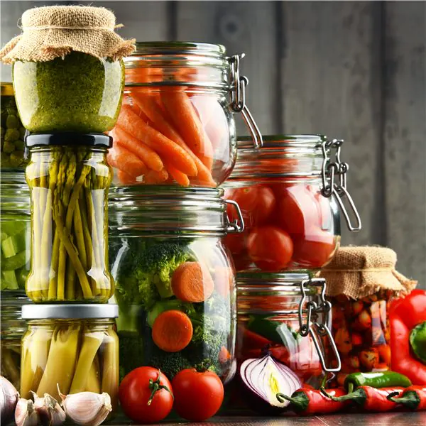 Vasi di vetro con verdure marinate e ortaggi freschi